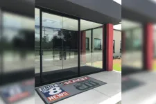 Thumbnail for Glass entrance doors with KNOE 8 News and local TV station logos on the floor mat outside a building.