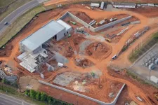Thumbnail for Aerial view of a construction site with a partially completed building and surrounding red earth roads