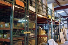 Thumbnail for Warehouse storage with metal shelving holding boxes and wooden panels under industrial roof lighting.