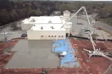 Thumbnail for Aerial view of concrete pouring at construction site next to a white building and parking lot with trees in the background