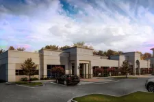 Thumbnail for Modern commercial office building with beige facade, parking lot, trees, and cloudy sky at dusk.