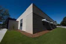 Thumbnail for Modern single-story commercial building with gray brick walls, large windows, and green lawn under a clear blue sky.