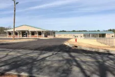 Thumbnail for Newly constructed single-story building with green roof, large paved parking lot, and fenced area under clear sky.