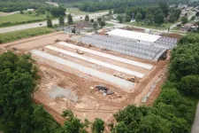 Thumbnail for Aerial view of a construction site with foundation slabs and steel framework surrounded by greenery and nearby roads.