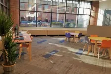 Thumbnail for Bright modern workspace with computers, colorful chairs, round tables, large windows, and a potted plant.