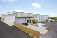 Thumbnail for Modern warehouse with loading docks, trucks, and fenced parking area under a blue sky.