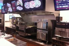 Thumbnail for Modern pizza restaurant kitchen with digital menu boards and stainless steel ovens and equipment.