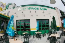 Thumbnail for Outdoor seating area at Best Wings USA restaurant with green chairs, tables, and colorful umbrellas on a sunny day.