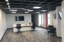 Thumbnail for Modern office reception area with wooden floor, black chairs, white desk, and wall-mounted TV screens.