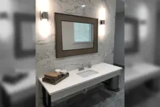 Thumbnail for Modern bathroom vanity with white countertop, rectangular sink, framed mirror, and marble wall tiles with sconces.