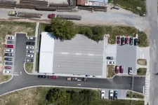 Thumbnail for Aerial view of a large building with multiple parked cars and green trees surrounding the area.