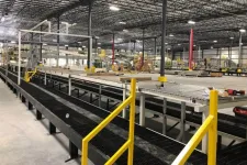 Thumbnail for Interior of a large industrial warehouse with conveyor belts and yellow safety railings under metal roof lights.