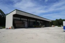Thumbnail for Large open metal storage shed housing construction materials and forklifts on a sunny day with clear blue sky.