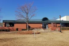 Thumbnail for Brick building with green roof, leafless trees, and dry grass under clear blue sky on a sunny day
