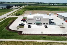 Thumbnail for Aerial view of Alexander building with parking lot, surrounding greenery, and rural landscape under blue sky.