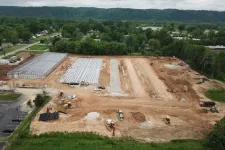 Thumbnail for Aerial view of a construction site with machinery, foundation work, and surrounding greenery.