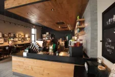 Thumbnail for Cozy modern coffee shop interior with wooden accents, barista at counter, and customers seated by framed artwork.