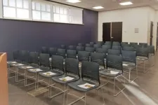 Thumbnail for Empty conference room with rows of black chairs and papers on seats, ready for an event or presentation.