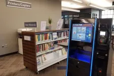 Thumbnail for Library book return kiosk next to bookshelves of new materials and a printers/copiers station.