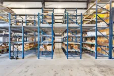 Thumbnail for Spacious warehouse interior with blue metal shelves stocked with boxes and a hand truck on concrete floor.
