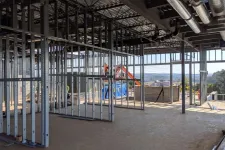 Thumbnail for Interior construction site with metal framing, exposed ceiling ducts, and large windows overlooking outdoor scenery.