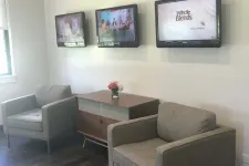 Thumbnail for Modern waiting area with two gray armchairs, wooden cabinet, three wall-mounted TVs, and a small flower vase.