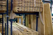 Thumbnail for Stacks of wooden planks and doors stored on metal racks inside a woodworking factory warehouse.