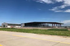 Thumbnail for Construction site with steel frame building and adjacent warehouse under blue sky and scattered clouds