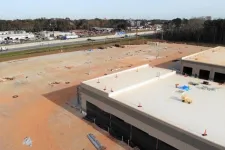 Thumbnail for Aerial view of a large construction site with two partially built commercial buildings and empty paved area near a highway.