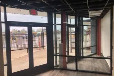 Thumbnail for Empty commercial space with glass doors and windows, wood flooring, and visible exit sign.