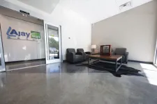 Thumbnail for Modern office lobby with leather chairs, wooden coffee table, and Ajay Group logo on glass wall.