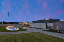 Thumbnail for Modern building with illuminated circular sculpture and flags under a vibrant blue and pink evening sky.