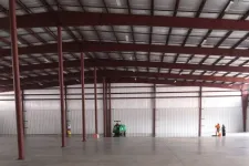 Thumbnail for Large empty warehouse interior with steel beams, concrete floor, and two workers operating cleaning equipment.