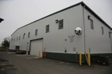 Thumbnail for Exterior view of a large white industrial warehouse with multiple windows and a loading dock door.