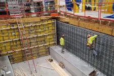 Thumbnail for Construction workers in safety gear installing steel reinforcement inside a concrete foundation with yellow formwork panels.