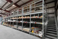 Thumbnail for Industrial warehouse metal shelving with wooden pallets, construction materials, and a staircase alongside the racks.