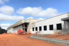 Thumbnail for Construction site with a large industrial building under development and orange dirt ground under a blue sky.