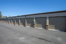 Thumbnail for Row of closed beige storage unit doors along a paved driveway under clear blue sky.