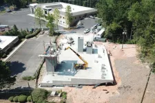 Thumbnail for Aerial view of a construction site with concrete foundation, crane, and workers amidst surrounding trees and buildings.