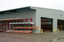 Thumbnail for Exterior view of a metal storage building with open bays and lumber racks on a gravel lot