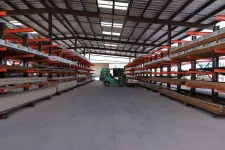 Thumbnail for Warehouse interior with metal and wood materials stored on orange racks and forklifts in the center aisle.