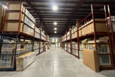 Thumbnail for Spacious warehouse aisle with tall red metal racks filled with cardboard boxes and packaged goods under bright ceiling lights