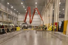 Thumbnail for Workers using concrete pump trucks inside a large industrial warehouse with high ceilings and pillars.