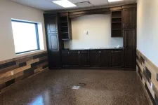 Thumbnail for Empty room with polished concrete floor, wood panel walls, large window, and dark wooden cabinets against the wall.