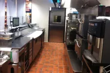 Thumbnail for Commercial kitchen with stainless steel appliances, ovens, sinks, and terracotta tiled floor under bright lighting.