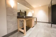 Thumbnail for Modern public restroom with wooden vanity, large mirror, tiled floor, and black partition stalls under bright lighting