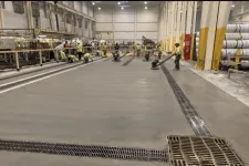 Thumbnail for Workers smoothing and finishing a large concrete floor inside an industrial warehouse with heavy machinery.