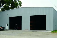 Thumbnail for Large gray metal warehouse building with two open garage doors and a parked vintage truck outside under trees.