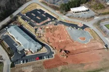 Thumbnail for Aerial view of a construction site with a paved parking lot, building, and earthmoving equipment working on red soil.