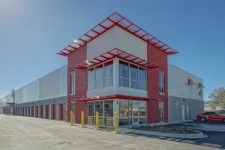 Thumbnail for Modern commercial building with red and gray exterior, large windows, and adjacent parking under clear blue sky